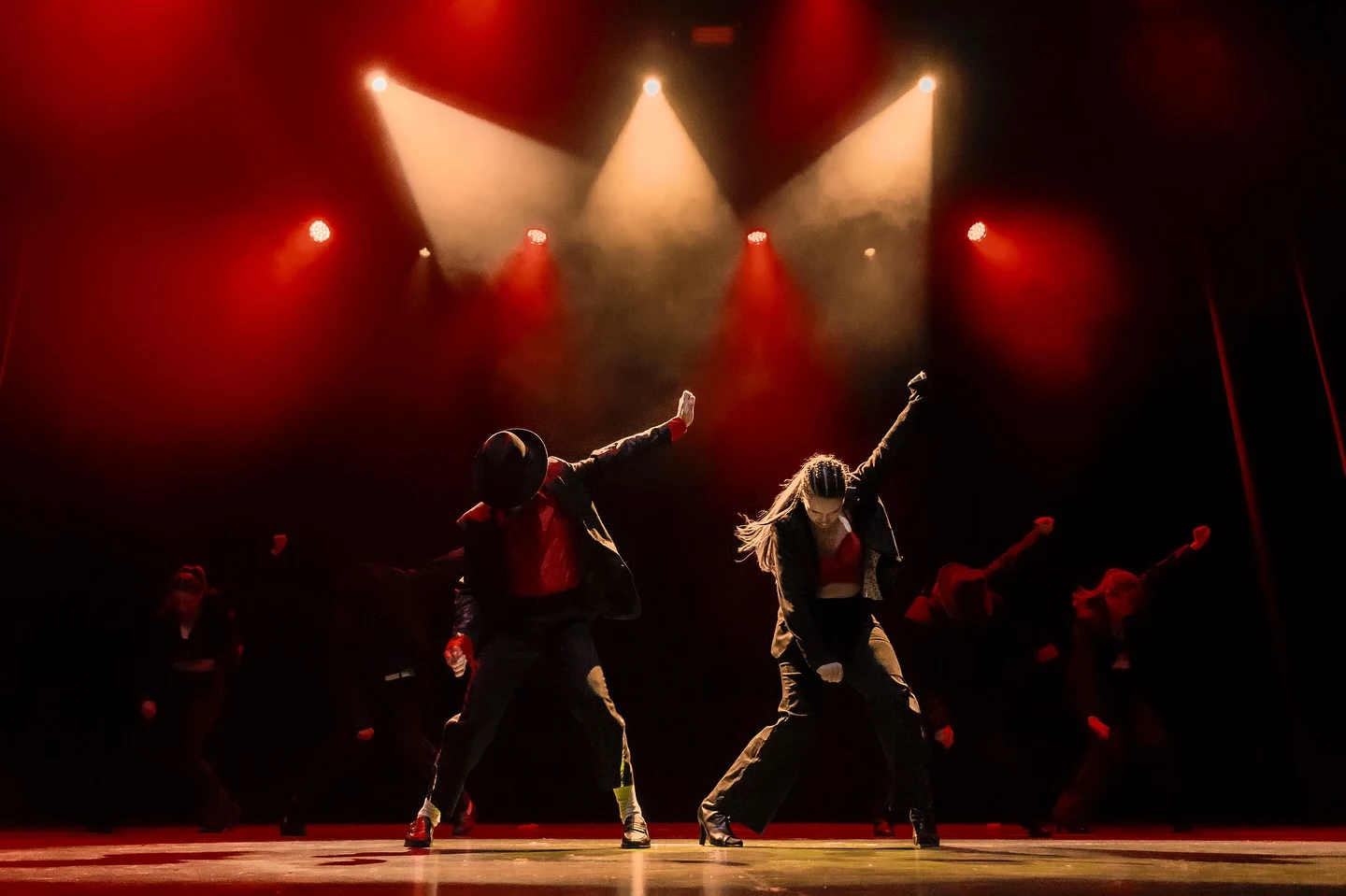 Bailarines extienden los brazos bajo luces rojas y cálidas